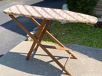 Side angle view of the wooden ironing board showing the padded strawberry-pattern fabric cover and the foldable wooden legs
