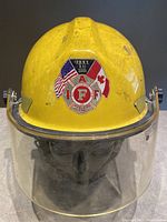 Front view of yellow Bullard Firedome firefighter helmet showing 9/11 commemorative fire department sticker with American and Canadian flags, clear visor lowered.