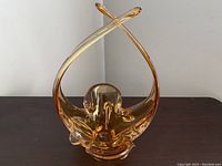 Front view of amber art glass basket showing crossing elongated stretch handles and rippled basket opening.