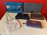 Photo showing six handbags, purses, and wallets arranged on a light wood surface against a red background.