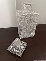 Side view of the square crystal glass decanter showing detailed pinwheel and diamond cut pattern with the stopper placed beside it.