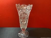 Front view of the tall clear cut crystal vase showing detailed daisy flower petal pattern and scalloped top edge.