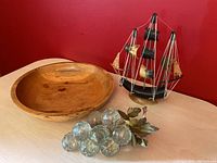 Photo showing the turned beech wood bowl, miniature ship, and crackle glass grapes with leaves on a light wood surface against red wall.