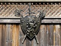 Front view of the vintage medieval lion coat of arms shield with sword and two battle axes mounted on a wooden fence.