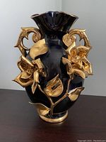 Front view showing ornate gold floral and leaf design on black glass with gold-trimmed wide flared top and dual handles.