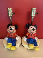 Pair of Mickey Mouse nightlight lamps on a flat surface showing full front view with red wall background.
