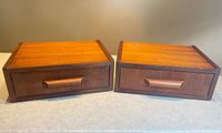 Front view of two teak floating side tables with one drawer each, showing wood grain and drawer handles.