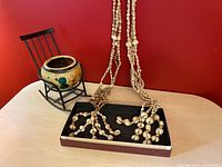 Photo showing two vintage shell macrame plant hangers with natural beige shells arranged in clusters and tassel ends, displayed alongside a small ceramic planter held by black metal miniature rocking chair frame.