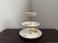 Front view of the three tier dessert serving cake stand with floral decorated porcelain plates and brass support rod.
