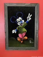 Full frontal photo of the vintage velvet painting featuring Mickey Mouse in vibrant colors on a black velvet background framed in rustic wood.