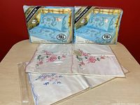 Two sealed Tastemaker Sheraton full size sheets (fitted and flat) with blue floral patterns in original packaging, standing upright on table.
