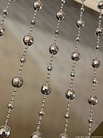 Close-up view showing vertical strands of shiny silver faceted disco ball beads alternating with smaller round beads on silver strings.