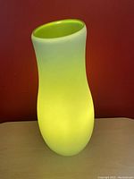 Side view of the lamp lit, showing frosted white glass with glowing lime green interior and curvy shape.