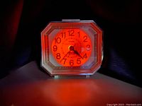 Vintage lighted electric alarm clock illuminated with orange-red light showing time in dark.
