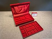 Photo showing open red jewelry box with two removable velvet trays and red alarm clock.