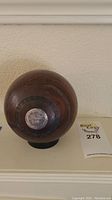 Top-view photo showing the wooden lawn bowl with affixed silver-colored metal plaque and the lot number card next to it.