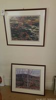 First photo showing two framed prints hanging on a wall and standing on the floor below it, depicting natural landscapes.