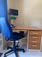 Blue adjustable office chair in front of the wood veneer desk with four drawers and white handles, showing general condition and style.