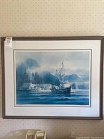Front view of the framed print depicting a boat and coastal village with misty mountains.
