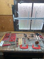Full layout of hand tools including Kromedge tap and die set, hand saw, clamps, hammers, hand drills, and rulers on workbench.