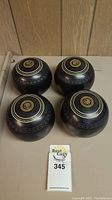 Four black vintage Henselite lawn bowls arranged in a square showing top branding and logo details.