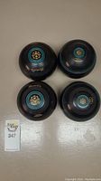 Four black lawn bowls with turquoise rings and gold emblems arranged on a surface, showing overall condition and number of items.