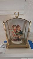 Porcelain Hummel figurine of two children inside a brass and glass display case