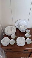 Johnson Brothers china set featuring 10-inch dinner plates, bowls, side plates, saucers, and green cups arranged on wooden furniture.