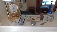 Full lot displayed including gold-tone Seiko clock, pewter dish with embossed fish lid, stone foo dog, small glass hummingbird, enamelled bookmark in box, and small metal bottle opener and metal pin