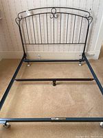 Front view of black metal queen bed frame with headboard showing vertical bars and scroll detailing.