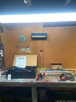 Workbench showing assortment of tools, carpenter's level, carpenter squares, hand saw, and carrying case.