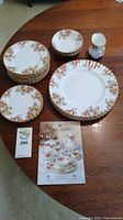 Overview photo of entire dinnerware set including plates, bowls, creamer, and product brochure.