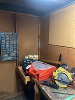 Workbench area with Black and Decker circular saw, orange toolbox with translucent lid, blue storage cases, and black drill case.