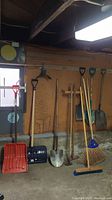 Full view of all tools leaning against wall including shovels, rake, broom, and hoe.