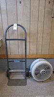 Photo of the black metal Milwaukee hand truck with curved handle and loading plate next to the vintage Seabreeze Turbo-Aire fan on carpet.
