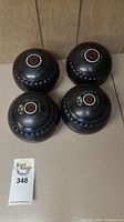 Four black vintage Thomas Taylor lawn bowls arranged together showing top logos and textured design.