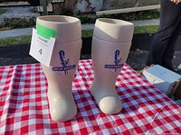 Two off-white ceramic pots shaped like boots, each with blue Steamwhistle logo on side, placed on red and white checkered cloth outdoors.