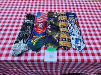 Photo showing all 5 collectible graphic ties laid out on a red and white checkered surface. Each tie features a distinct pop culture character or theme: Blondie & Dagwood, Superman, Mickey Mouse, Disney, Sonic.
