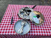 Photo showing the egg poacher pan with lid, the small pan with forks inside, and wire whisk on a red and white checkered cloth.