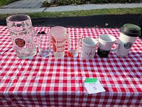 Front view of all glasses and mugs on checkered cloth outside.