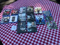 Top-down photo showing 15 DVDs and Blu-ray films arranged on a red and white checkered fabric surface. Multiple James Bond films visible in DVD cases, some loose discs without cases shown.