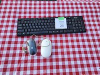 Black wireless keyboard with numeric keypad and two Apple wired mice (black and white) on a red and white checkered cloth.