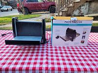 Nostalgia Bacon Express unit and original retail box shown side by side on a red and white checkered tablecloth outside.