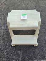 Top and side view of off-white plastic step stool with ridged steps and slightly dirty surfaces on asphalt ground.