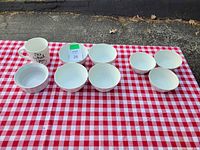 Photo showing the top view of seven white bowls and one white mug arranged on a red and white checkered tablecloth.