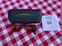 Pair of Serengeti sunglasses with black hard case placed on red checkered cloth.