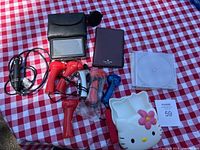 Photo shows all the travel-related items on a red and white checkered cloth including the Garmin GPS, mini fans, CD cases, Hello Kitty bento box, Kate Spade holder, and car charger.