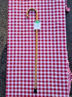 Full length view of the wooden walking stick on a red and white checkered cloth showing the entire stick and curved handle.