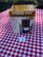 Waring Pro 4-cup coffeemaker original box on red and white checkered tablecloth outdoors.