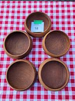Top-down view of five round wooden bowls arranged on red and white checkered tablecloth showing color and surface finish.